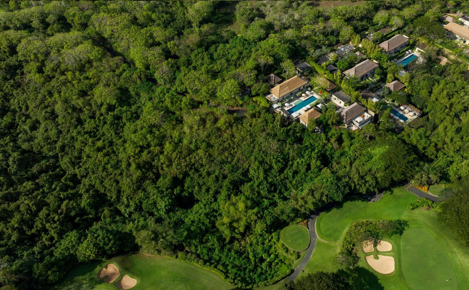 Вид сверху на Aman Villas at Nusa Dua: виллы с бассейнами в густом лесу над полем для гольфа