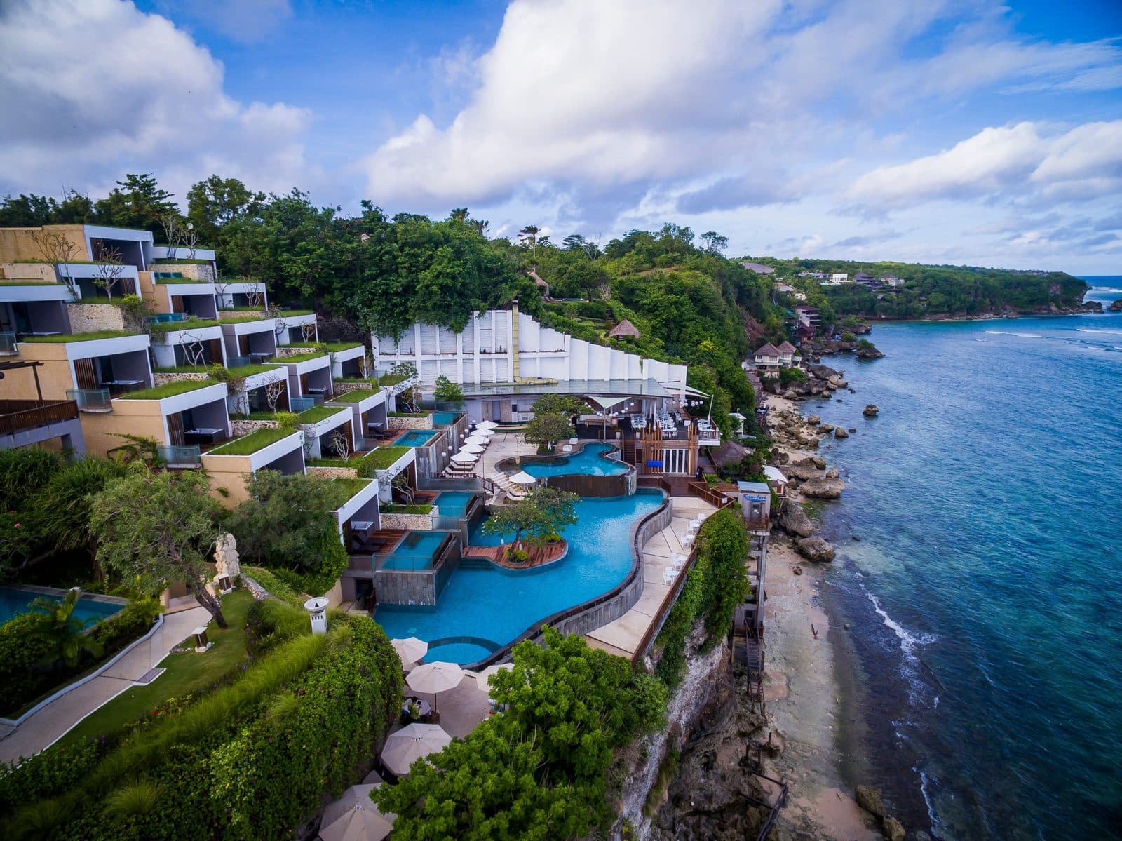Вид с воздуха на Svanata Uluwatu: корпуса уступами по склону, многоуровневый бассейн над обрывом и скалистый берег у океана