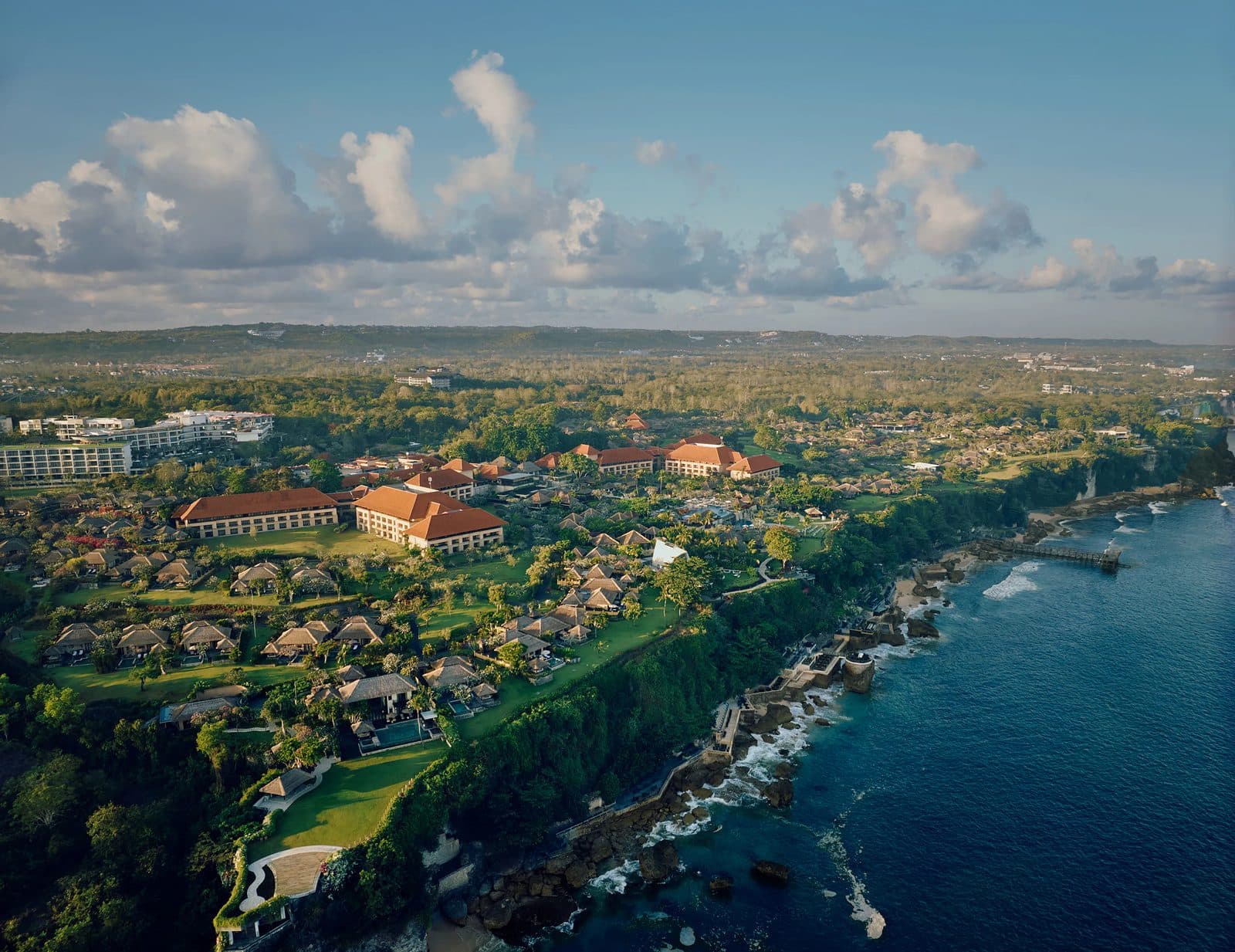Вид с высоты на AYANA Bali: корпуса под оранжевыми крышами и виллы в садах на краю утёса над океаном