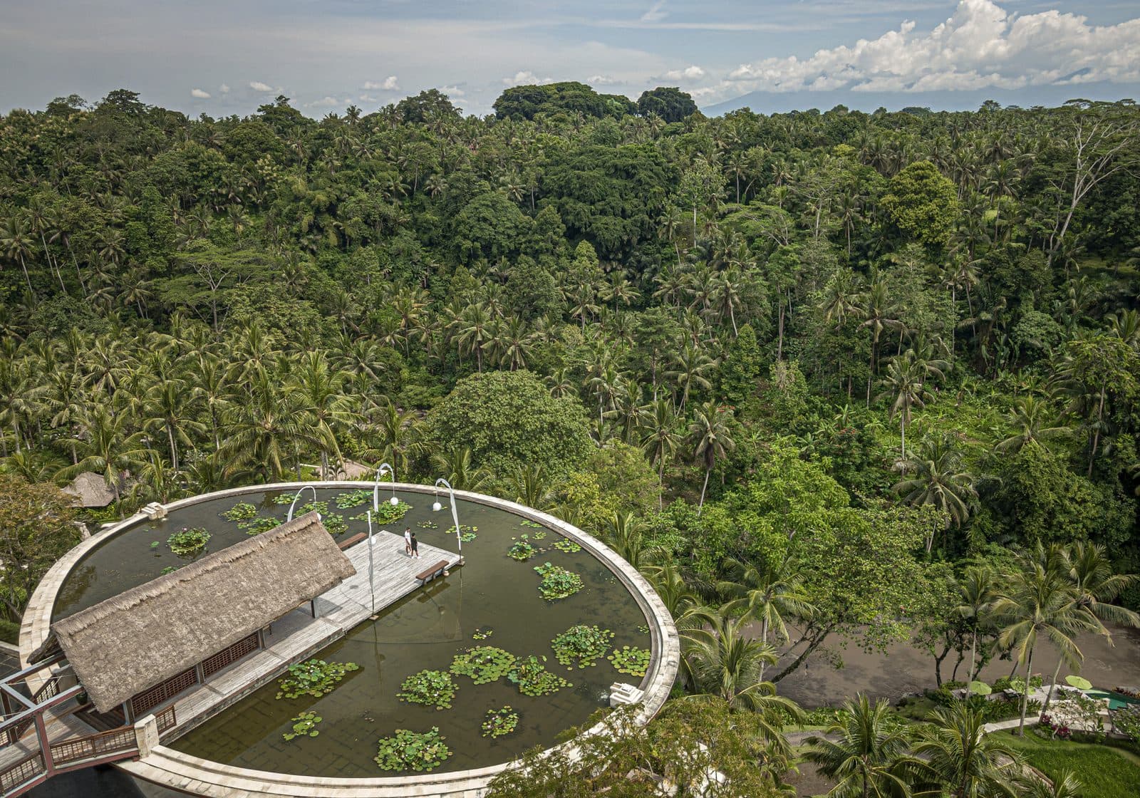 Aerial view of the circular rooftop lotus pond at Four Seasons in Sayan: a thatched pavilion and wooden bridge surrounded by the Ayung valley's forest