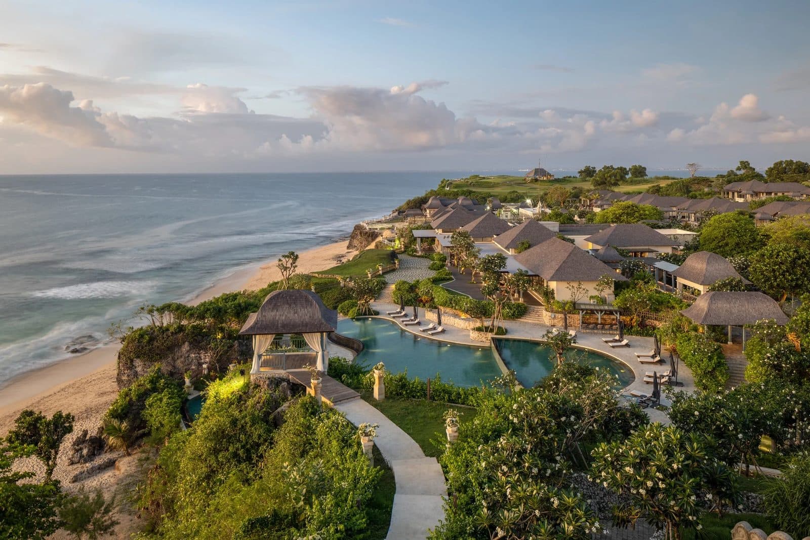 Jumeirah Bali на закате: виллы под тёмными крышами в саду над пляжем Дримленд, бассейн свободной формы и беседка на краю утёса