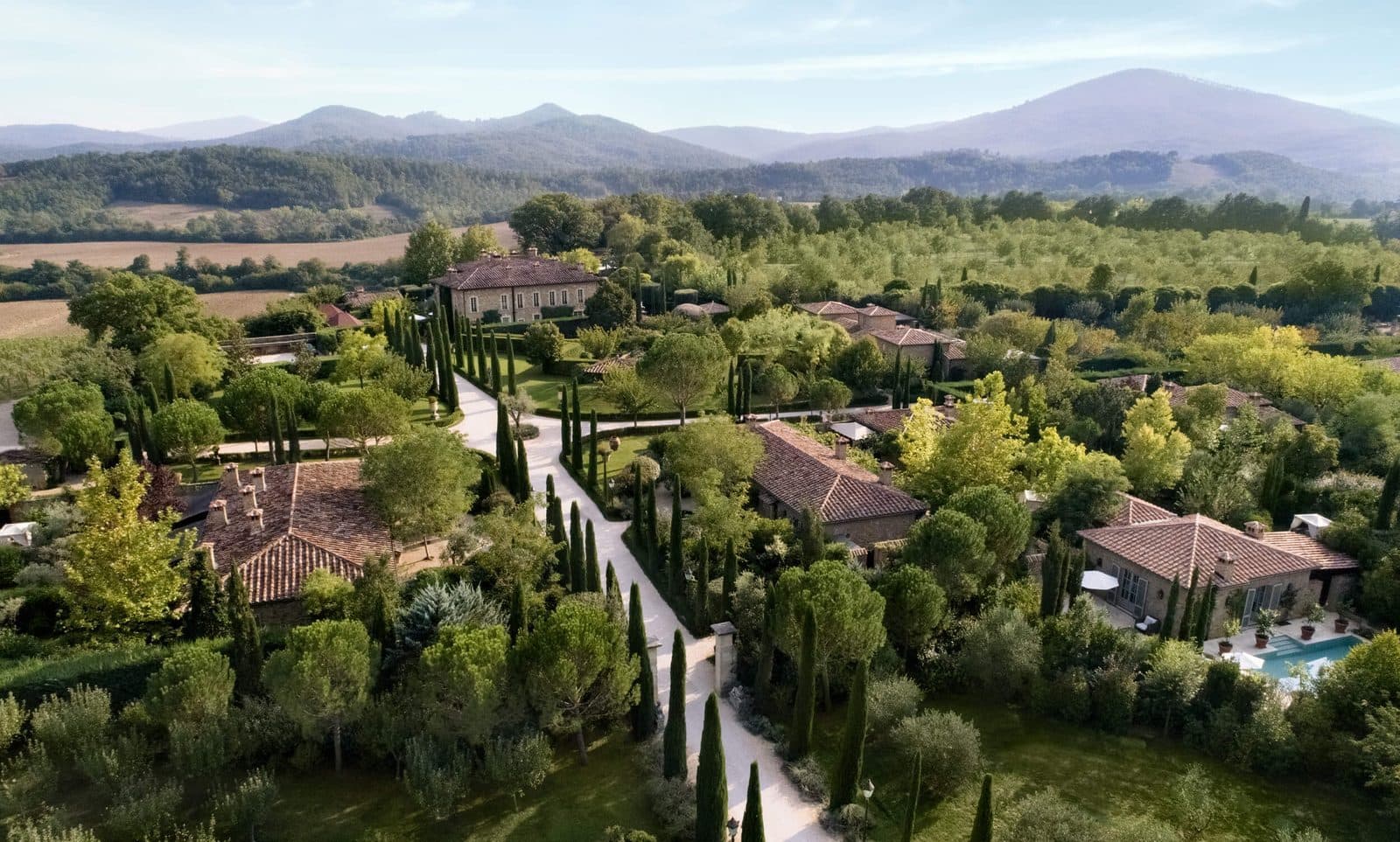 Aerial view of Borgo Santo Pietro buildings among gardens and cypresses against Tuscan hills