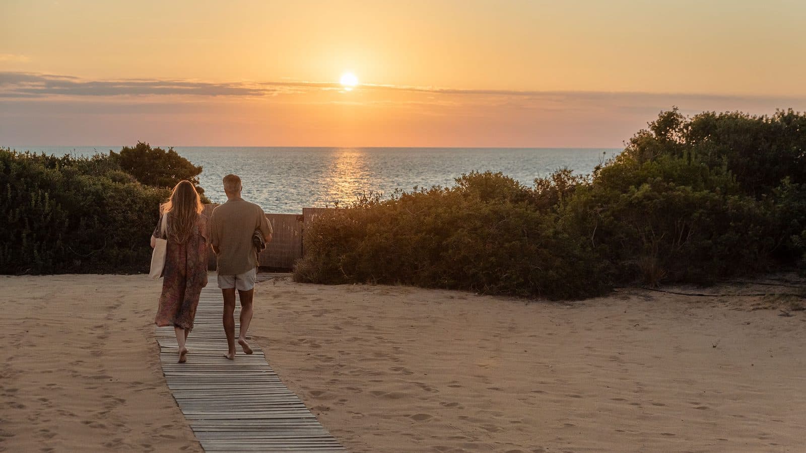 A path across a sandy beach to the Ionian Sea at sunset, with a couple walking along it