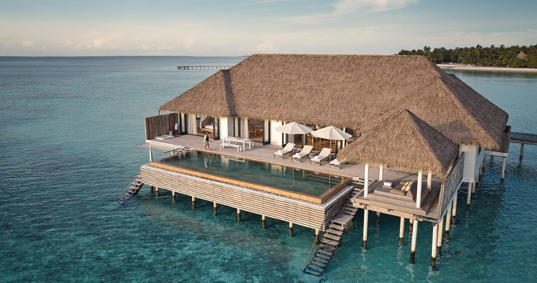 A thatched overwater villa with a long pool and terrace above the lagoon