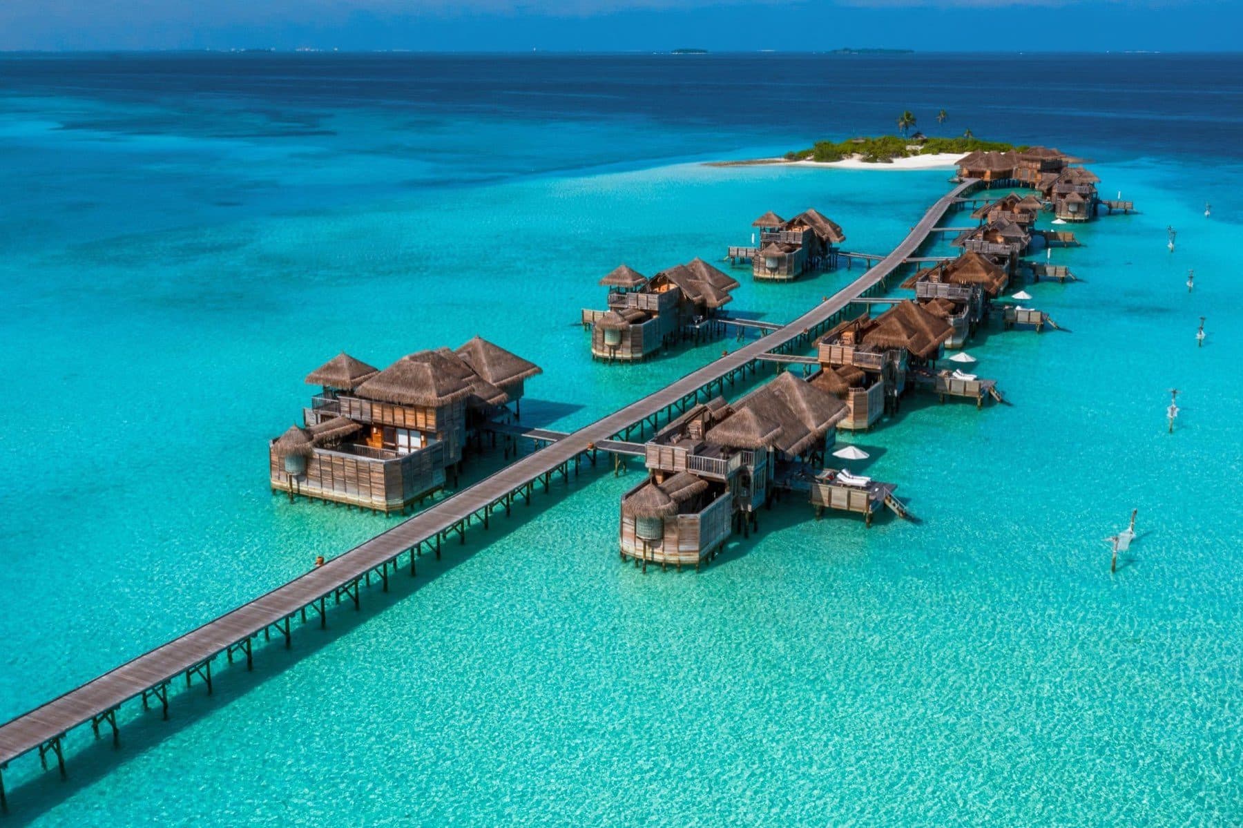 Aerial view of a wooden bridge and stilt villas amid a turquoise lagoon