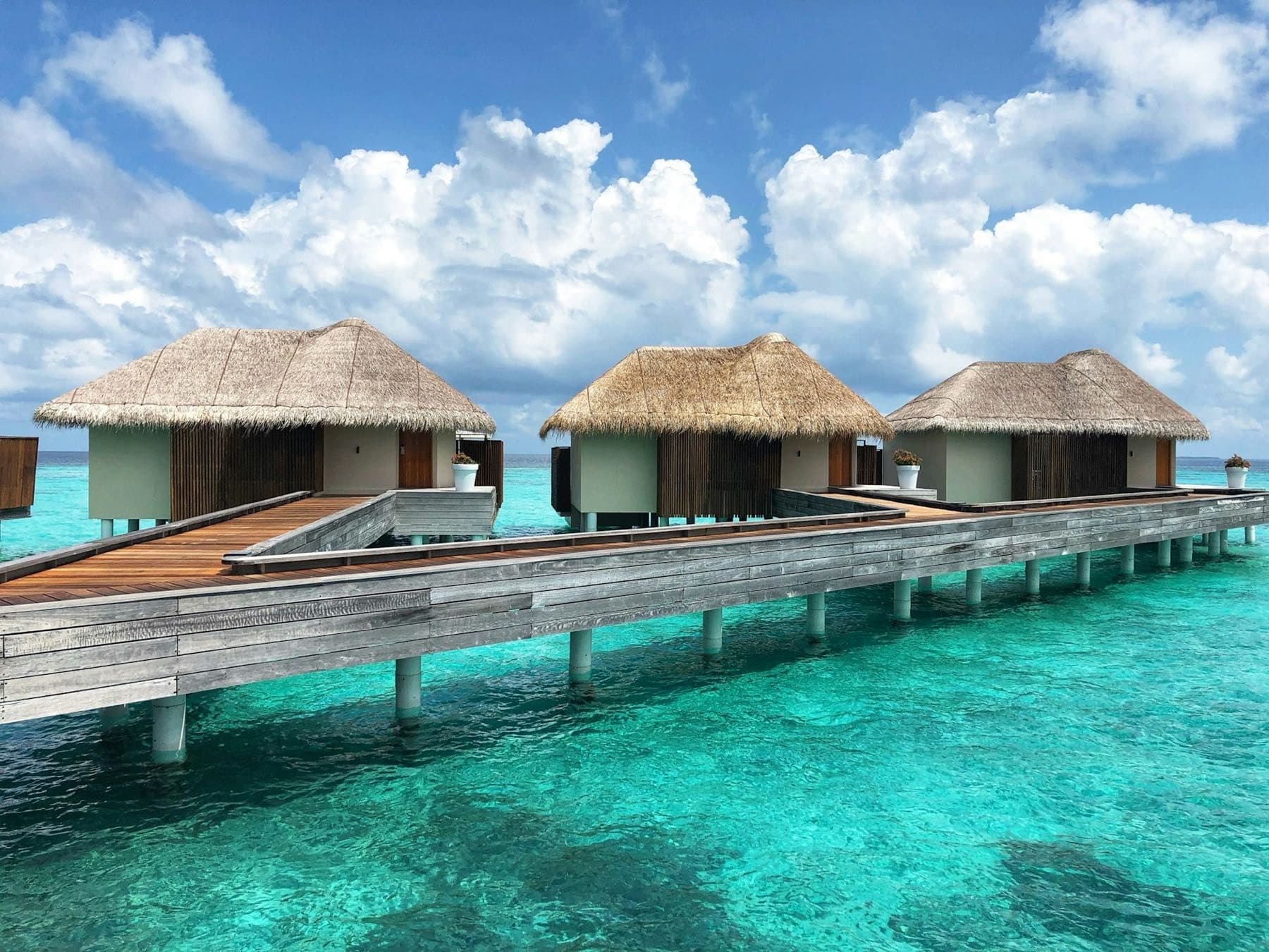 Three thatched stilt villas above a turquoise lagoon, reached by wooden walkways