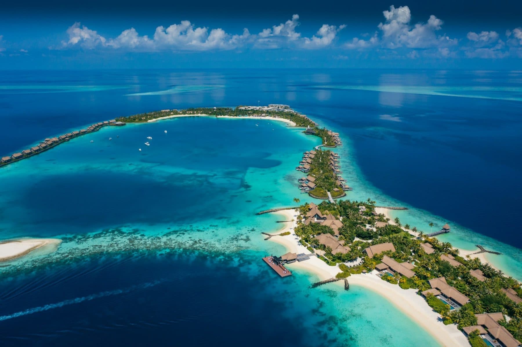 Aerial view of the resort islands: overwater villas along the reef, beaches and greenery, surrounded by the blue ocean