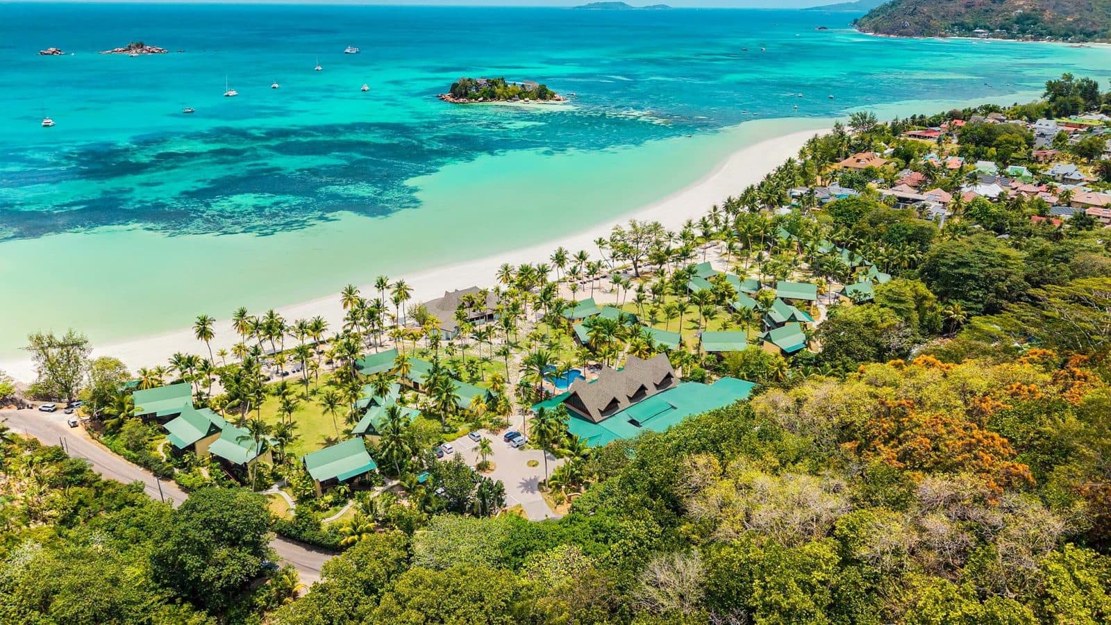 Вид с дрона на Paradise Sun: бунгало под зелёными крышами среди пальм вдоль белого пляжа Кот-д’Ор, бирюзовая вода и островок Сен-Пьер