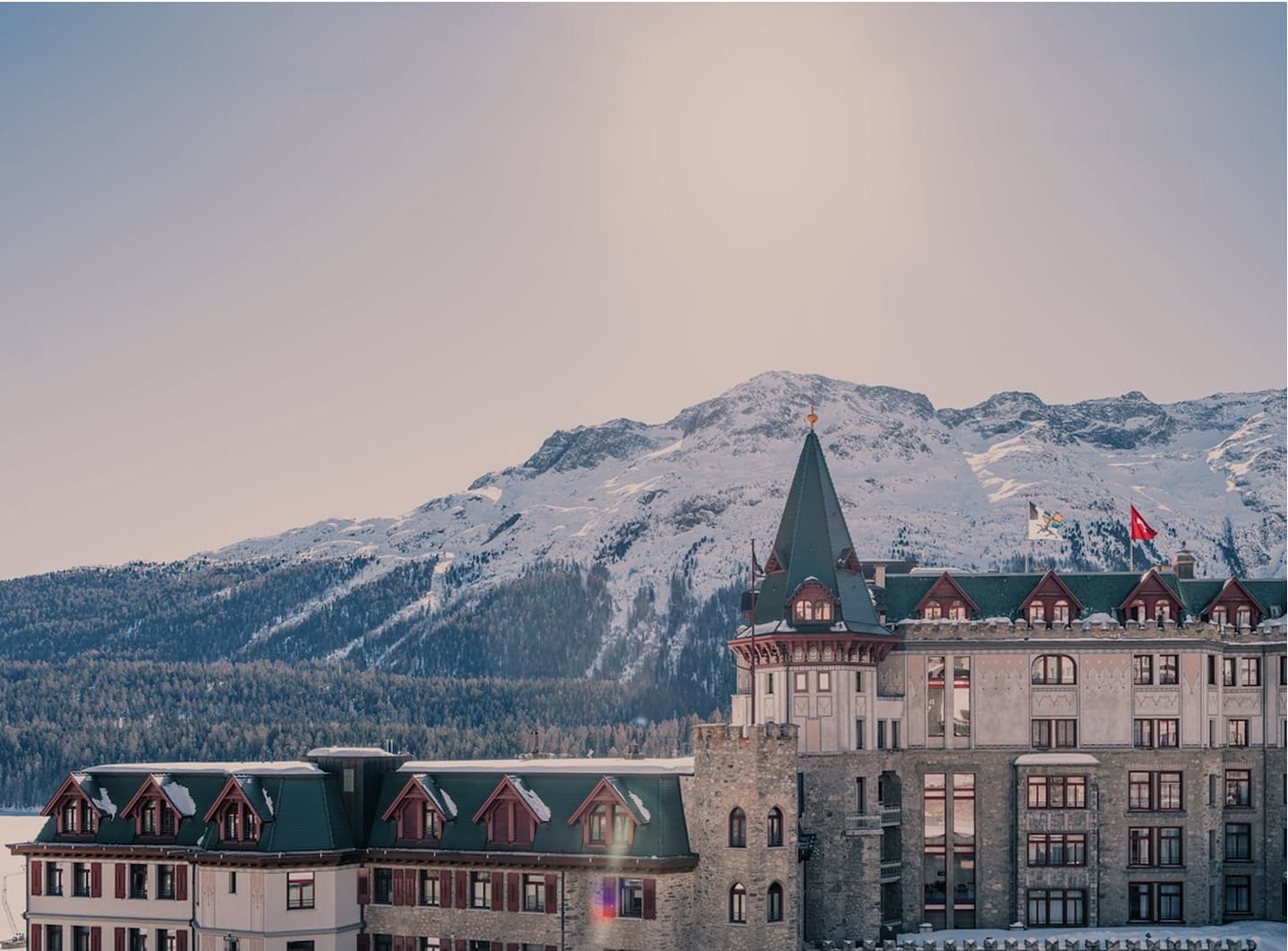 Башня и фасад Badrutt’s Palace перед заснеженными горами в утреннем свете