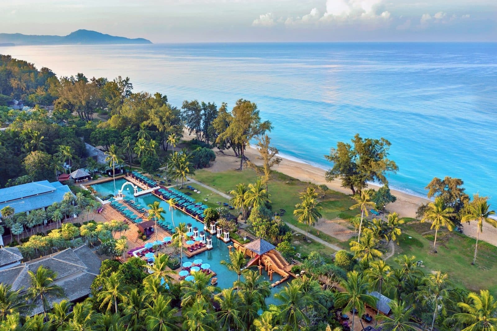 Вид сверху на JW Marriott Phuket: бассейны-лагуны среди пальм, газон и длинный пляж Май Као вдоль бирюзового моря