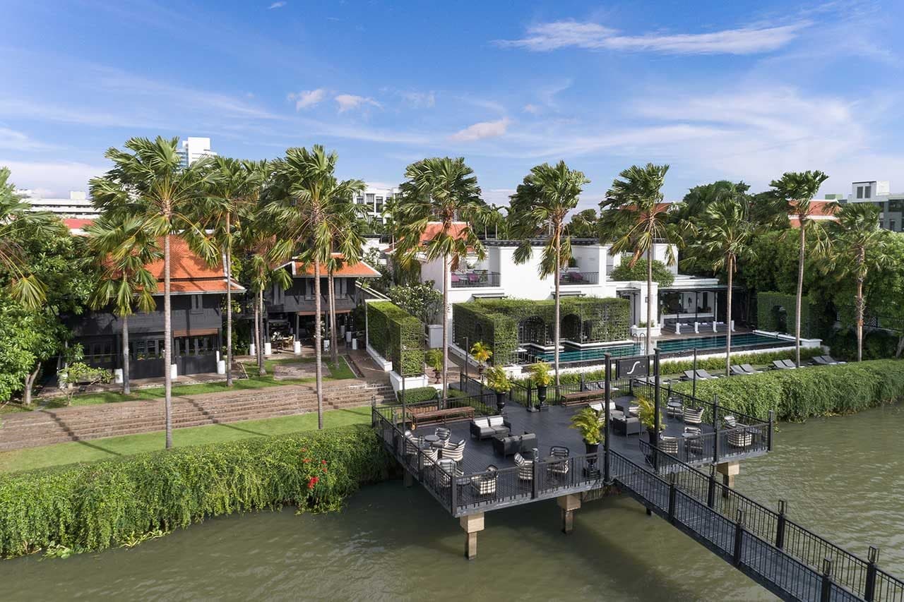 Aerial view of The Siam: a pier with armchairs above the Chao Phraya, palms, red-roofed teak houses and a long riverside pool