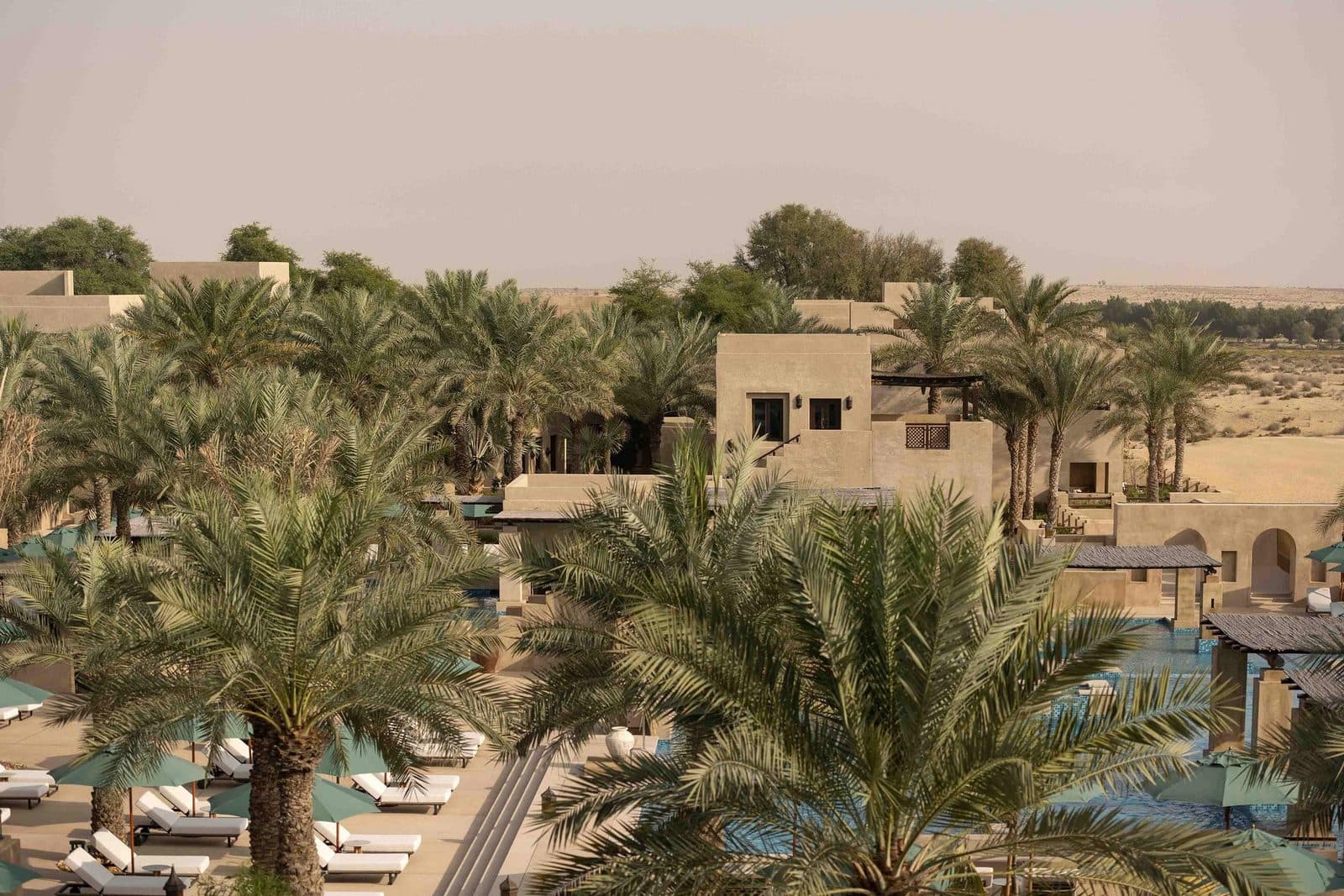 Bab Al Shams сверху: песочные здания среди финиковых пальм, бассейн с шезлонгами и пустыня за курортом