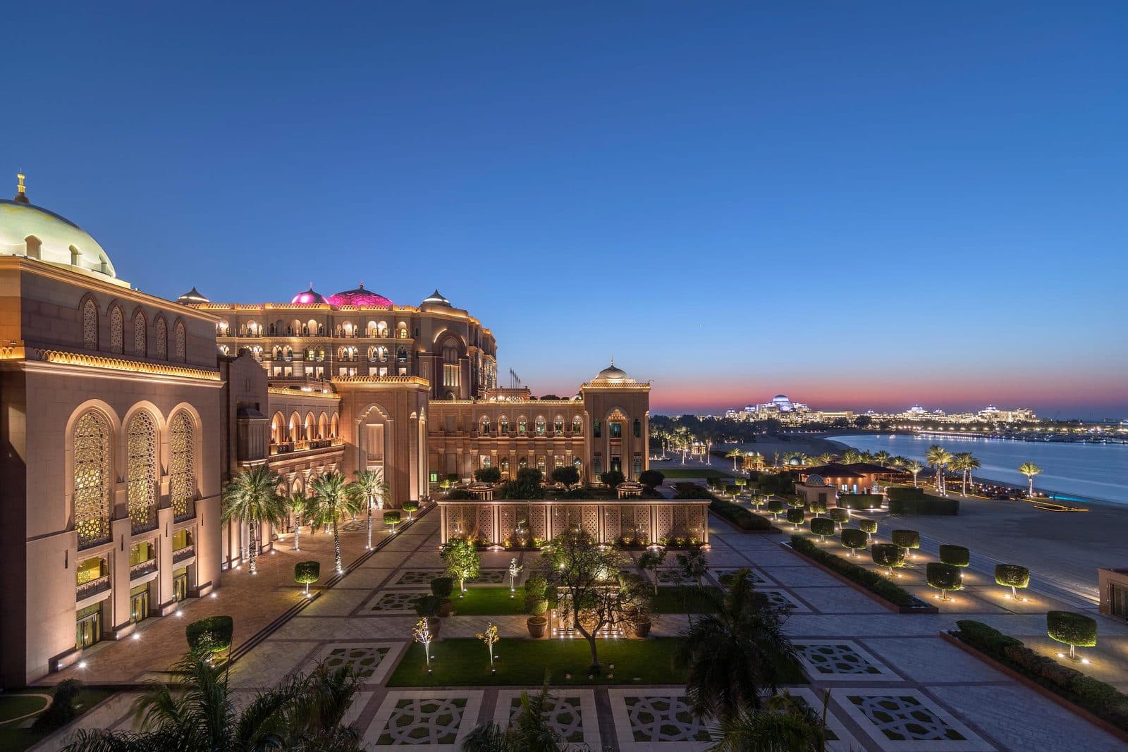 Emirates Palace в сумерках: подсвеченные арки и купола, сад с узорными дорожками и пляж у залива