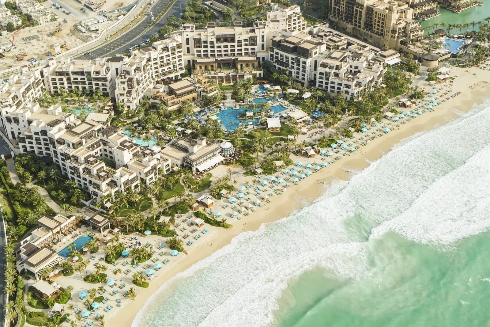 Jumeirah Al Naseem сверху: светлые корпуса среди пальм и бассейнов, пляж с голубыми зонтиками и белая полоса прибоя